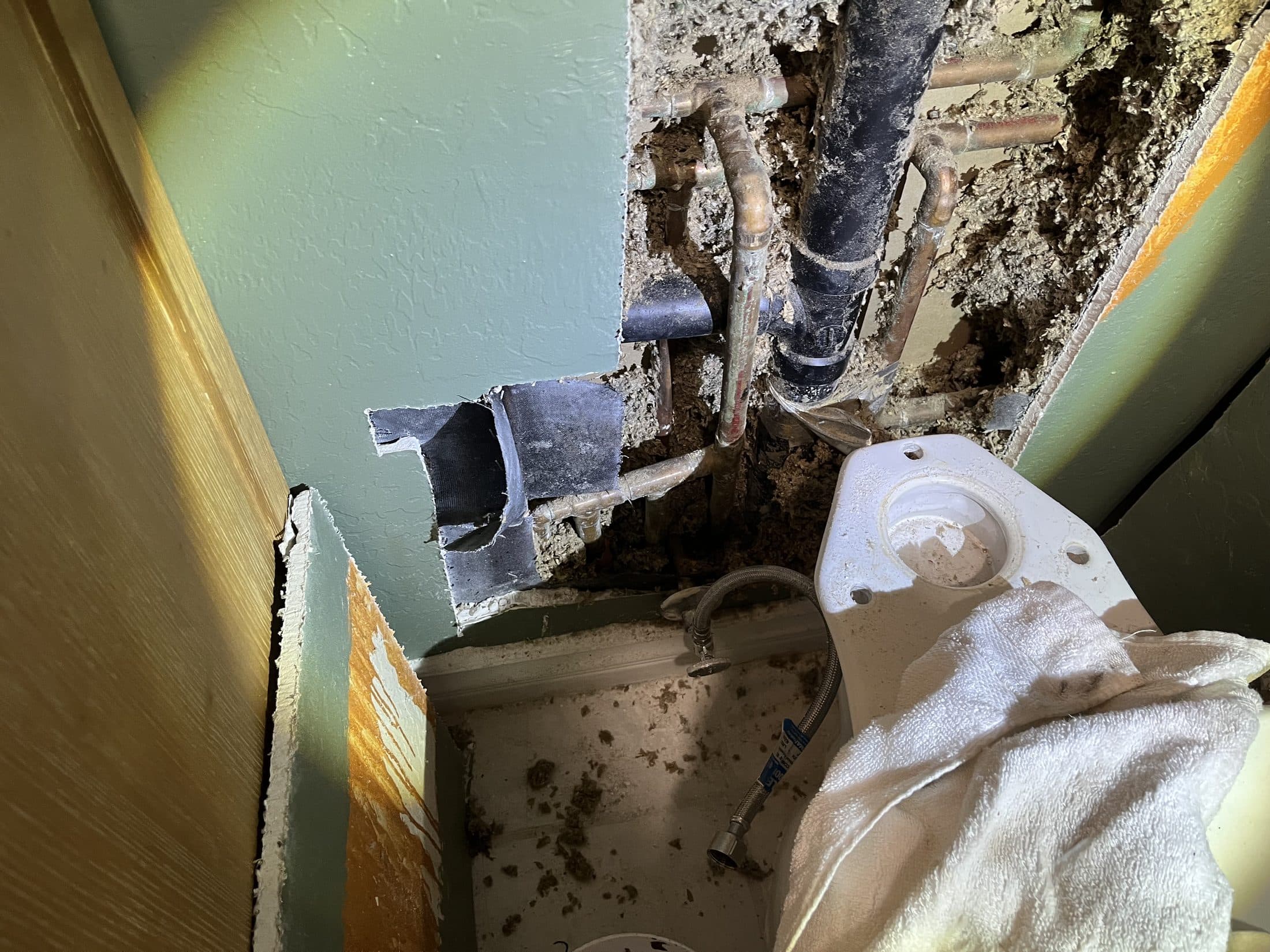 Bathroom wall opened above the toilet during a slab leak reroute, exposing the copper water lines and drain stack